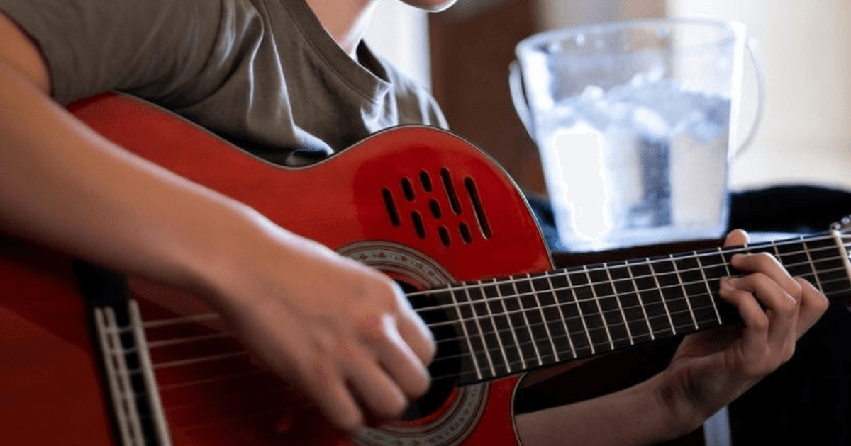 A young person playing guitar with a bucket of iced water